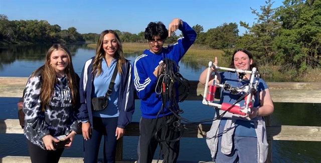 Students holding underwater robot at beach