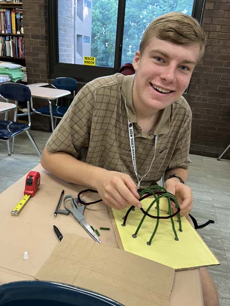 Student posing for picture with wigwams