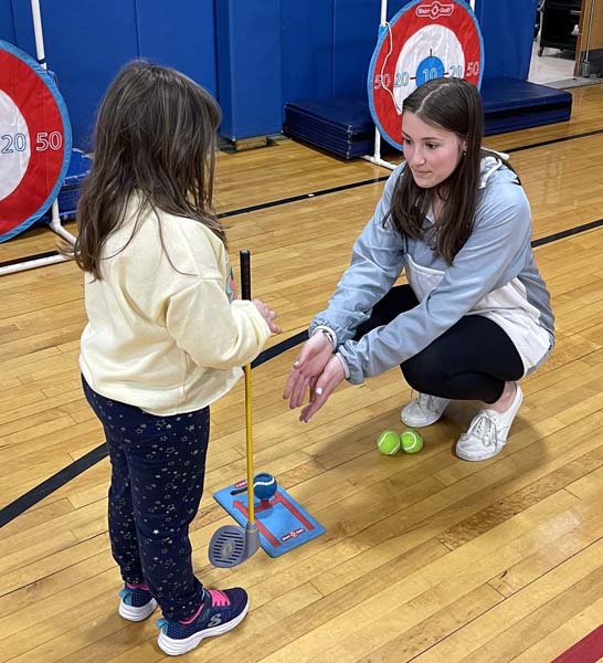 high school student helping younger student play golf